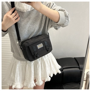 Detail of a black nylon crossbody bag with dual buckles and fashion logo shown on model