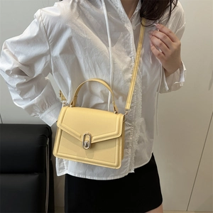 Minimalist light yellow leather crossbody bag with gold buckle shown on a model