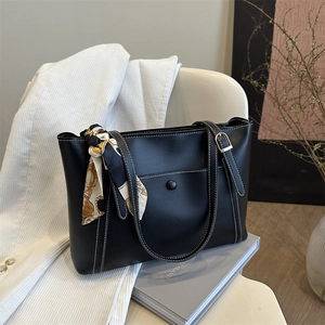 Black leather tote bag with white stitching and floral silk scarf on a chair