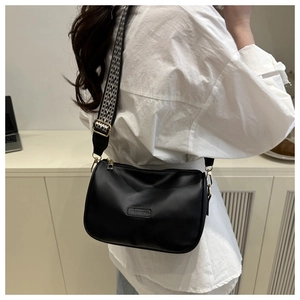Detail of black leather bag with wide geometric strap and embossed fashion text