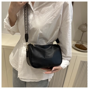 Close-up of black crossbody bag with a wide geometric strap and gold hardware