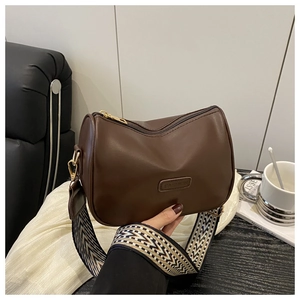 Detail of dark brown leather pillow bag with wide patterned strap and gold metal hardware