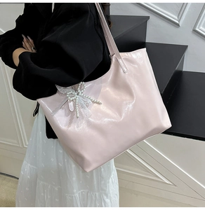 Detail of light pink tote bag with shiny leather texture and pearl bow charm