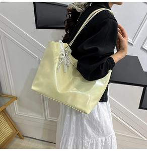 Detail of light yellow glossy tote bag with delicate white lace and pearl bow charm