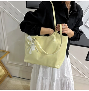 Macro shot of yellow PU leather tote bag with lace pearl bow charm and dual handles