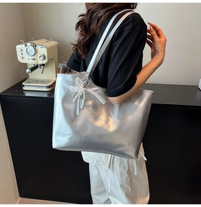 Detail of silver metallic tote bag featuring white lace bow and elegant pearl charm detail
