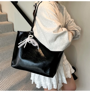Large black glossy tote bag with lace bow and pearl charm shown in street style photo