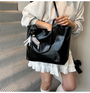 Detail of a large black tote bag with white lace bow and pearl charm on a model