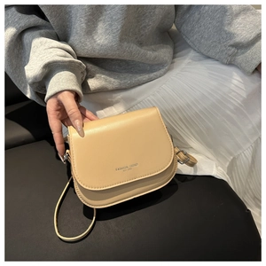 Detail of a beige saddle bag with Fashion Trend embossing worn over a grey knit sweater