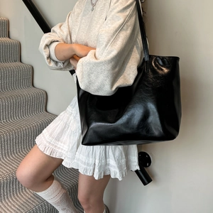 Minimalist black leather tote bag with glossy finish and long shoulder straps for women