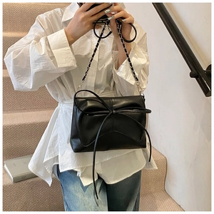Détail du sac en cuir noir avec grand nœud et bandoulière en chaîne sur mannequin