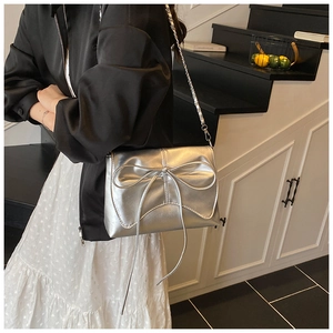 Detail van zilveren handtas met een grote decoratieve strik en ketting schouderband