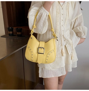 Detail view of yellow underarm bag with silver square buckle and rivet studs on shoulder strap