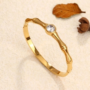 Elegant gold bamboo joint bangle with a sparkling center diamond on a textured surface