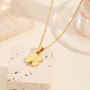 Collier trèfle doré avec texture de feuille sur un fond minimaliste de pierre beige