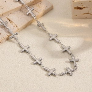 Detailed close-up of beaded silver cross pendant necklace on a cream textured surface