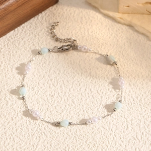 Elegante bracciale con perline, ciondoli a cuore e pietre blu su superficie bianca