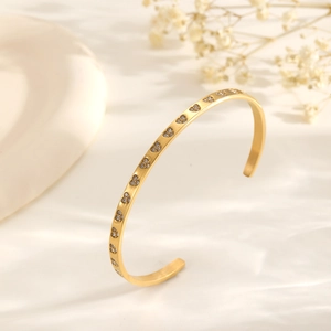 Exaggerated gold cuff bracelet with heart zircon inlay on white textured background