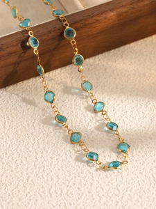 Detailed close-up of a gold chain necklace featuring sky blue oval bezel-set glass stones
