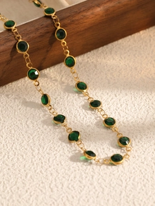 Detailed macro view of gold chain necklace featuring round green bezel-set crystals