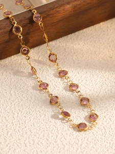 Macro detail of gold-tone chain necklace with bezel-set purple round faceted gemstones