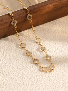 Detail of gold chain necklace featuring bezel-set round clear crystals on wooden stand
