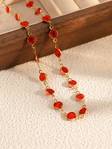 Close-up of golden necklace with faceted red crystals on a dark wood jewelry box
