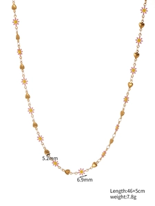 Détail macro des breloques marguerite et cœur sur un collier en acier inoxydable doré