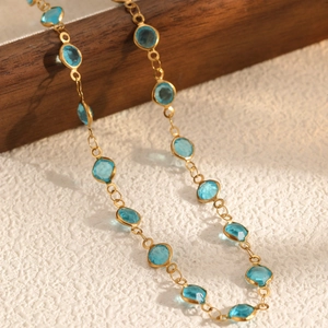 Elegant gold necklace with bezel-set blue round crystals on a luxury textured background