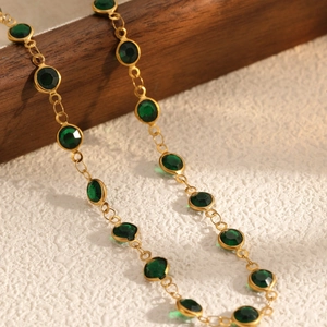 Elegant gold chain necklace with faceted emerald green gemstones on a wooden stand