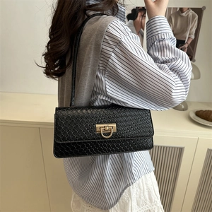Sac sous le bras noir à texture tissée avec boucle dorée porté à l'épaule par un mannequin
