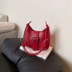 Minimalist red leather shoulder bag with silver eyelets and buckle on white books