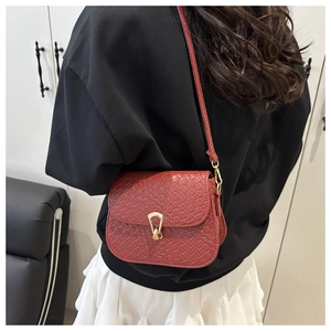 Detail of red-brown crossbody bag with woven texture and gold horseshoe buckle