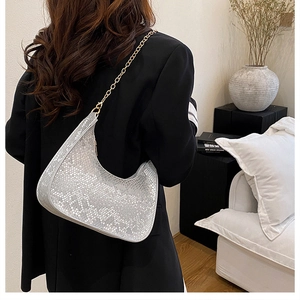 Detail of silver snake-pattern crescent bag featuring a textured finish and gold chain strap
