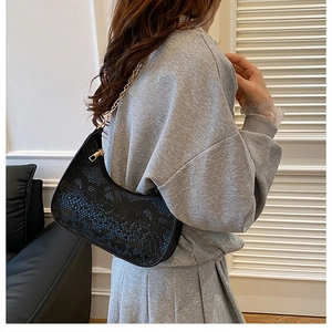 Detail of black faux snake skin bag with gold chain strap worn by a model