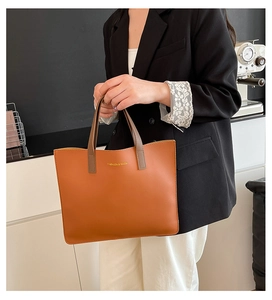 Detalle del bolso tote naranja vibrante con asas gris-marrón y logotipo dorado elegante