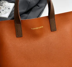 Detalle del asa del bolso de cuero marrón con letras doradas y costuras precisas
