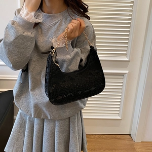Black snake embossed hobo bag with a gold metal chain strap shown in a lifestyle setting