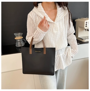 Detalle de un bolso tote negro con asas de cuero marrón llevado por una modelo en oficina