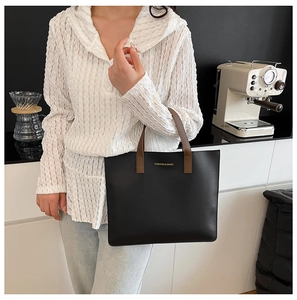 Detalle de bolso tote negro con asas marrones y letras doradas de moda