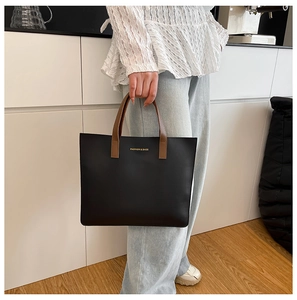 Detalle de un bolso tote negro grande con asas marrones y letras doradas de moda