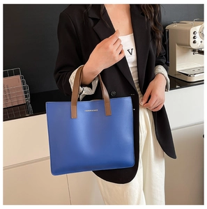 Detalle de bolso tote de cuero azul con asas marrones y letras doradas para el uso diario