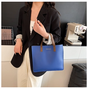 Primer plano de bolso tote de cuero azul con asas marrones y texto grabado