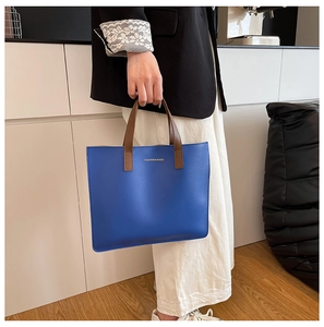 Detalle del bolso tote de cuero azul real con asas marrones y letras doradas de moda