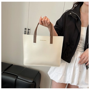 Detalle del bolso tote crema con asas marrón oscuro y logotipo dorado frontal