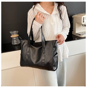 Close-up of black textured leather tote bag with wide shoulder strap on a modern table