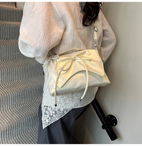 Détail du sac à bandoulière en satin blanc cassé avec nœud, perles et bord en dentelle