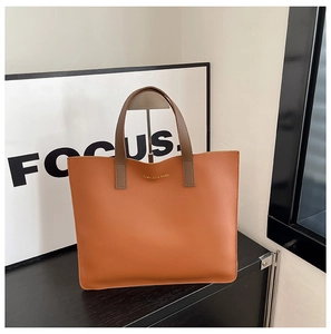 Detalle del bolso tote naranja-marrón con letras doradas y asas en color marrón oscuro