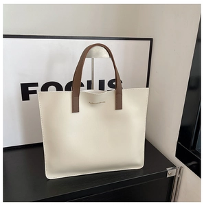 Detalle del bolso tote crema minimalista con asas marrones y texto dorado en relieve