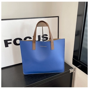 Detalle de bolso tote de piel azul granulada con letras doradas y asas marrones